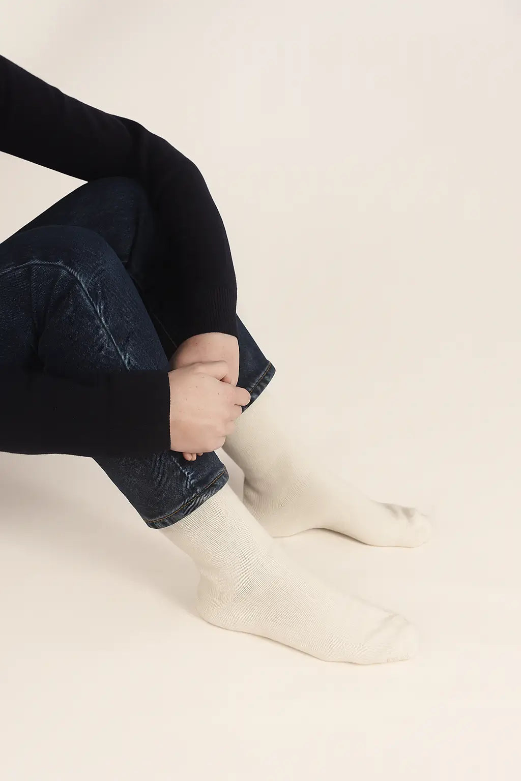 Person wearing dark jeans and white socks on a beige background