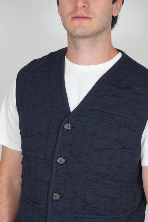 A man wearing a dark navy quilted vest over a white t-shirt, shown from the chest up against a light gray background.