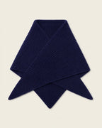 A folded ribbed knit scarf in deep navy blue, displayed on a solid light beige background.