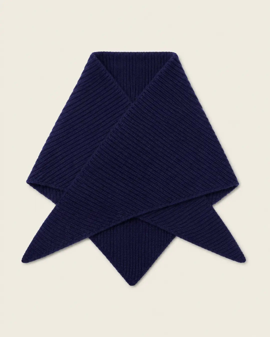 A folded ribbed knit scarf in deep navy blue, displayed on a solid light beige background.