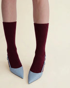 A person's legs wearing bordeaux ribbed crew socks with light blue pointed-toe heels, shown against a plain beige background.