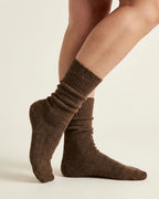 A close-up of a person's feet and lower legs wearing brown ribbed knit socks against a plain light studio background.