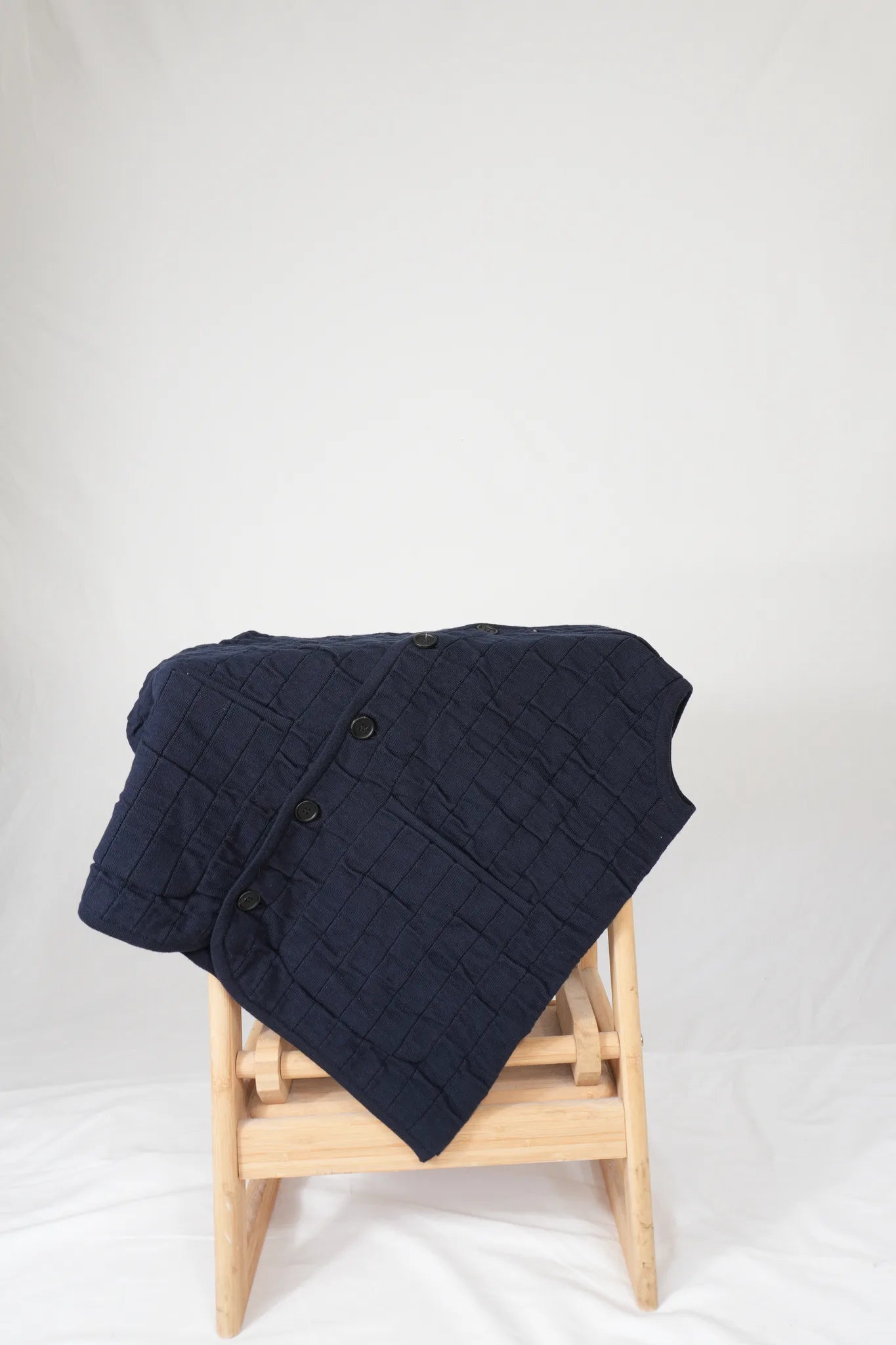half british cotton quilted knitted gilet in navy, draped over a wooden stool showing the quilted knit texture