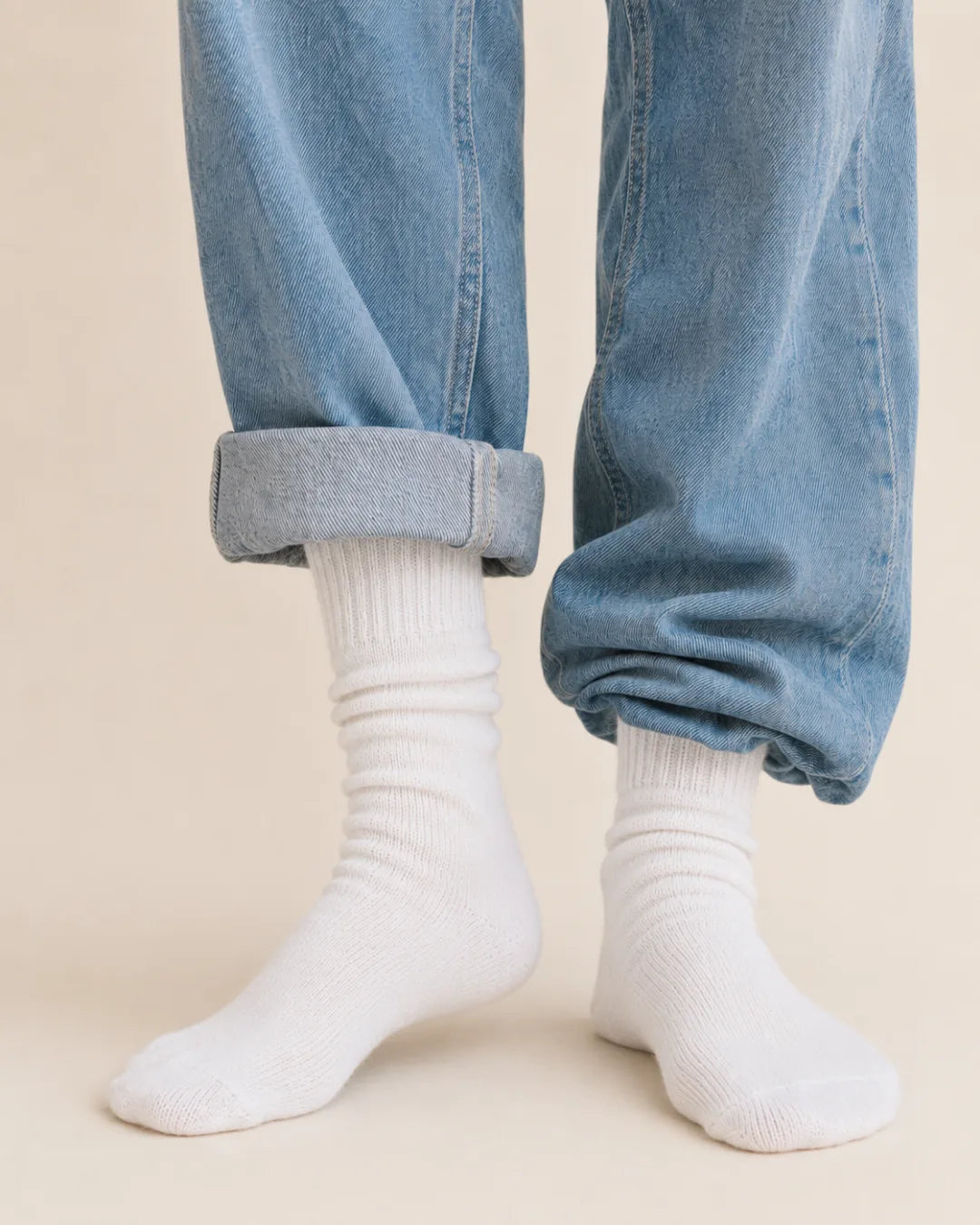 Cream ribbed crew socks worn with light cuffed jeans against a warm background.