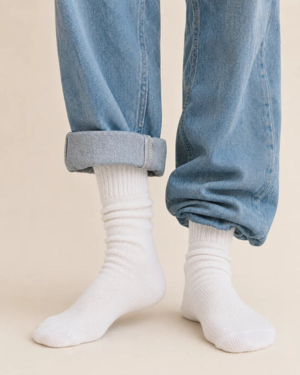 Cream ribbed crew socks worn with light cuffed jeans against a warm background.