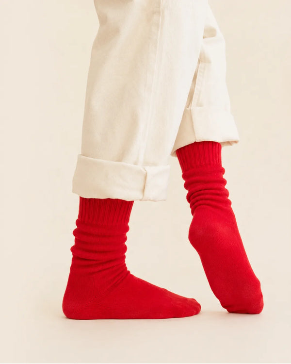A person wearing bright red crew socks with rolled-up pants, shown from the knees down against a plain light studio background.