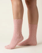 A pair of ribbed ankle socks in a dusty pink color, shown on a model's feet against a plain off-white background.